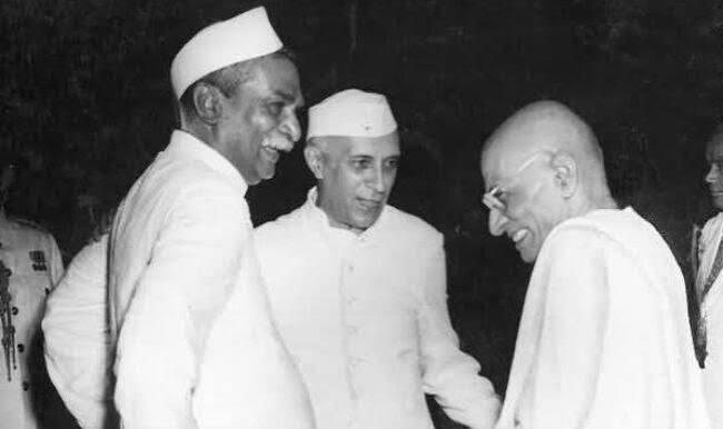 Rajendra Prasad and Jawaharlal Nehru, both in Gandhi caps, greeting a smiling C. Rajagopalachari at an official gathering.